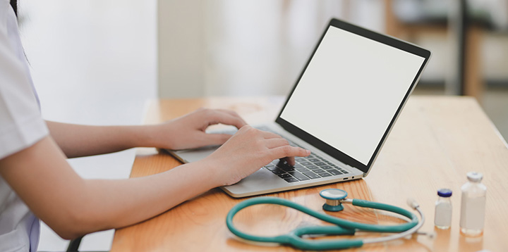 Close-up view of young female doctor examining the patient chart while using a laptop computer in her office.